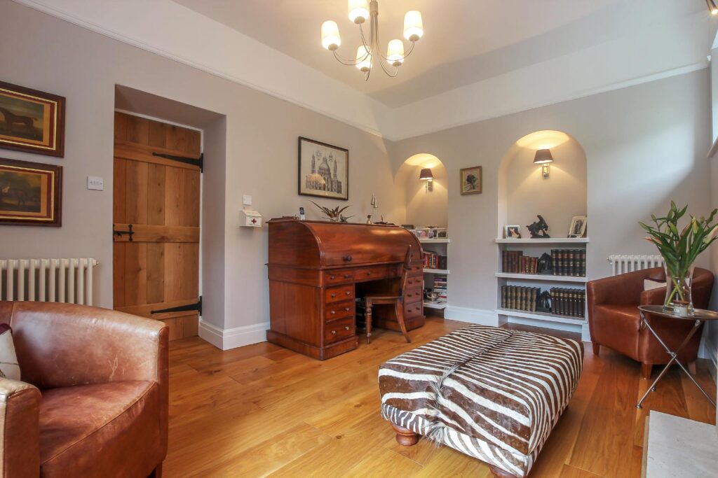 Home office with a rolltop desk, wooden floor and occasional seating