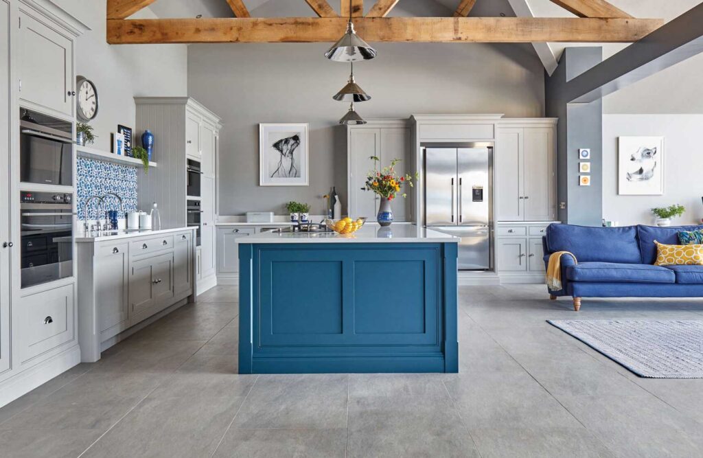 A neutral colour palette kitchen with soft grey tones on the flooring, walls and cabinetry with pops of blue colour from the island unit and sofa