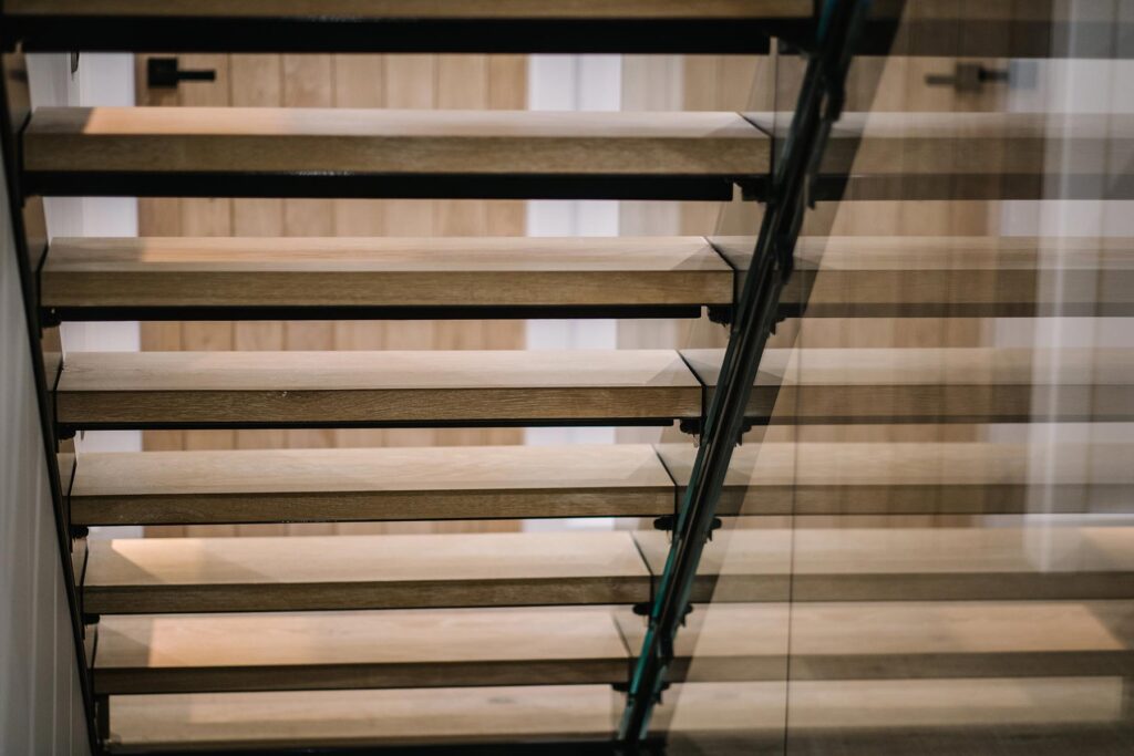 Close up of 1 flight of stairs with a juxtaposition of materials using a metal frame, wood treads and glass panelling