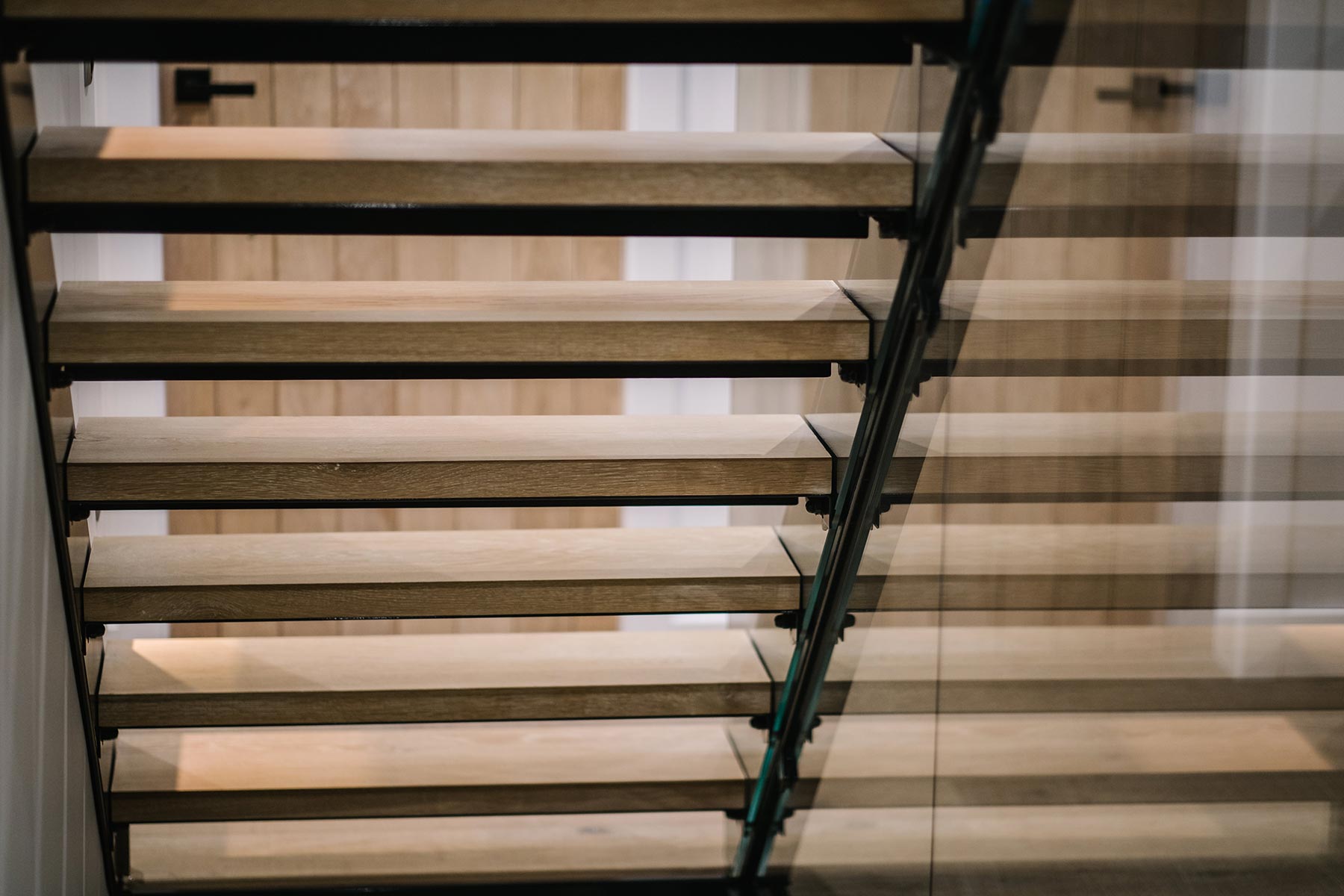 Close up of 1 flight of stairs with a juxtaposition of materials using a metal frame, wood treads and glass panelling