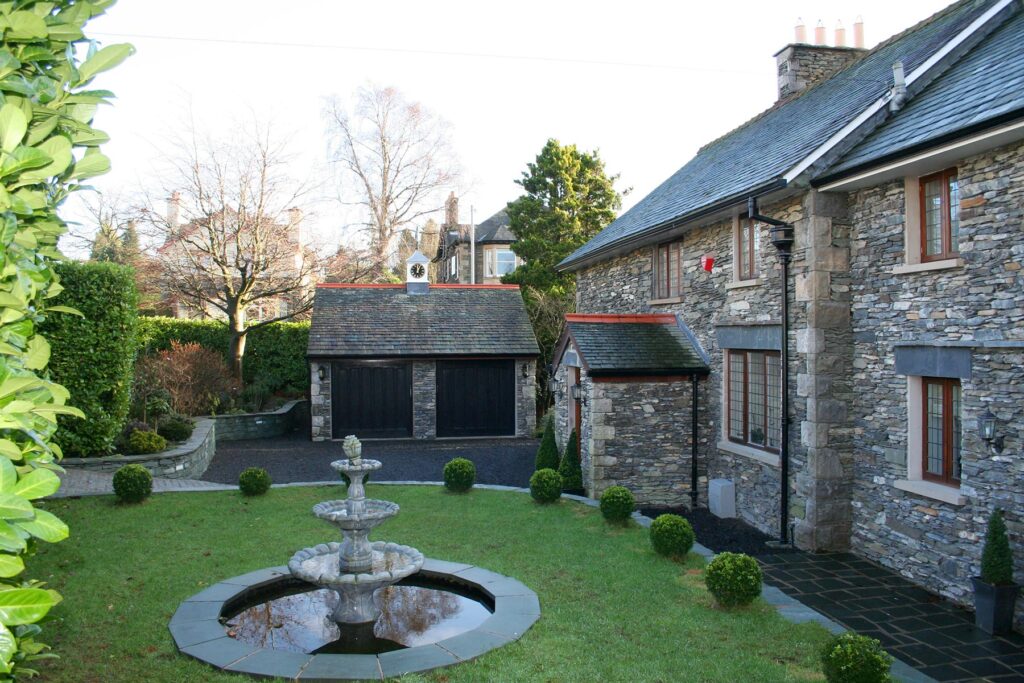 Exterior view of the front garden, stone garage block and stone built house as part of a full home renovation project in Windermere, Lake District