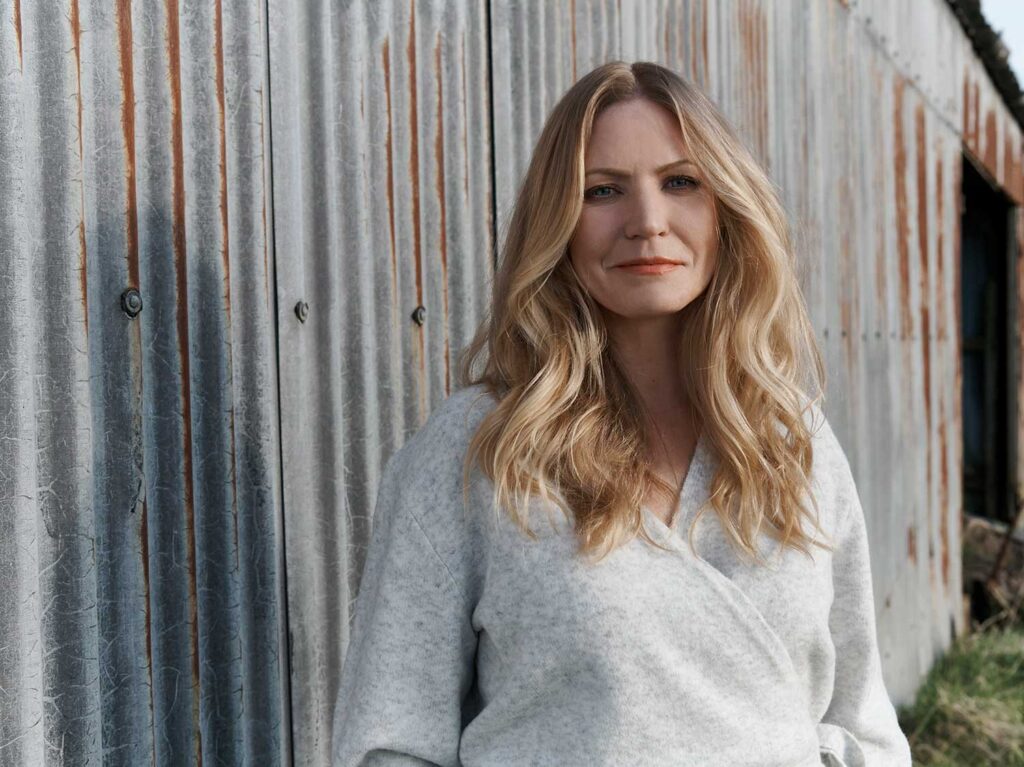 A close up of Charlotte Findlater, a luxury and high-end interior designer, standing by a corrugated barn