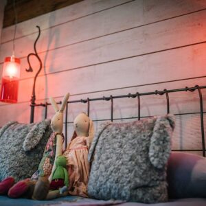 Close up of a double bed with cushions, hanging side lights and child toys
