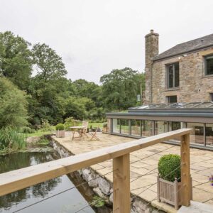 Exterior view of the bespoke kitchen orangery and stone patio next to the mill pond as part of a grade II Mill Renovation project