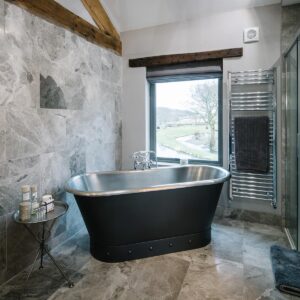 Master ensuite with floor and wall tiling and a rolltop bath with a view outside