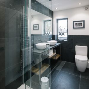 Bathroom with dark wall and floor tiles, walk in shower and white sanitaryware
