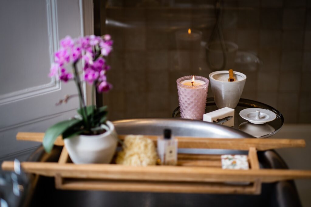 Close up of a table next to a bath with a lit candle and bath salts in a pot