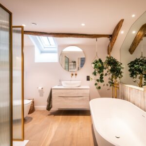 Biophilic designed ensuite bathroom with gold framed ribbed glass shower screen, white vanity unit, white bath and large wall mirror