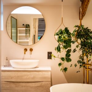 Biophilic designed ensuite bathroom with live hanging plants in oak bent baskets, white sink on a vanity unit with gold taps