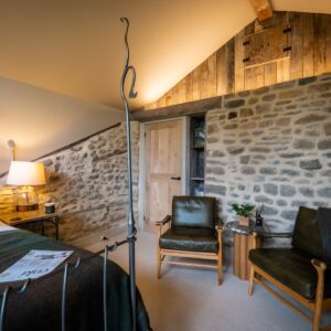Bedroom with a double bed side on, a seating area with two seats and an exposed stone wall with led lighting