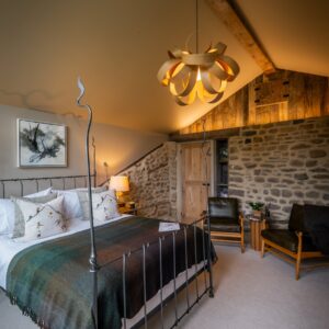 Bedroom with a double bed side on, a seating area with two seats and an exposed stone wall with led lighting