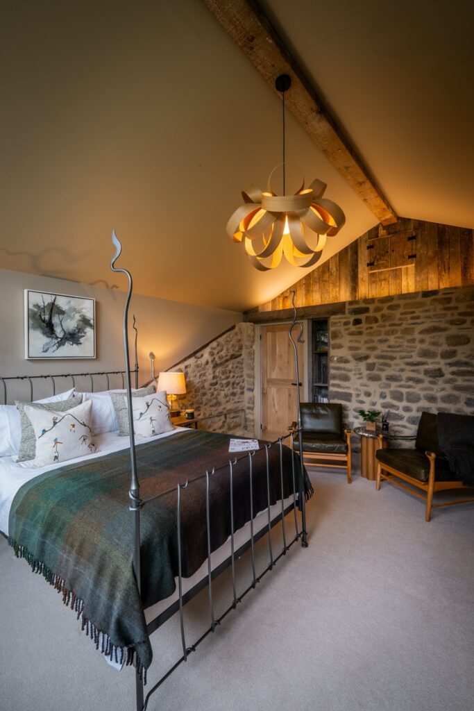 Bedroom with a double bed side on, a seating area with two seats and an exposed stone wall with led lighting