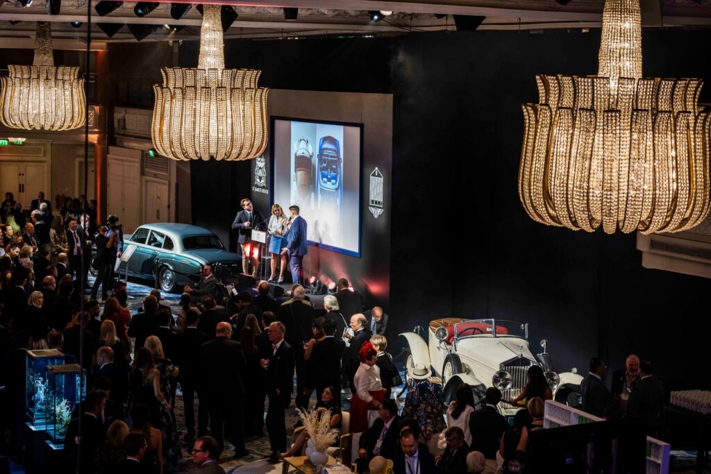 The Rolls Royce car club event with 2 vintage Rolls Royce cars either side of the stage with 3 people on
