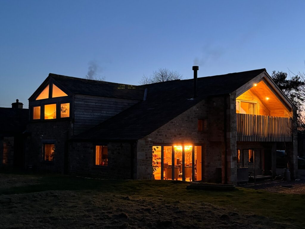 Evening shot of a stone built barn conversion in the Lake District with the internal lights on and balcony lights on