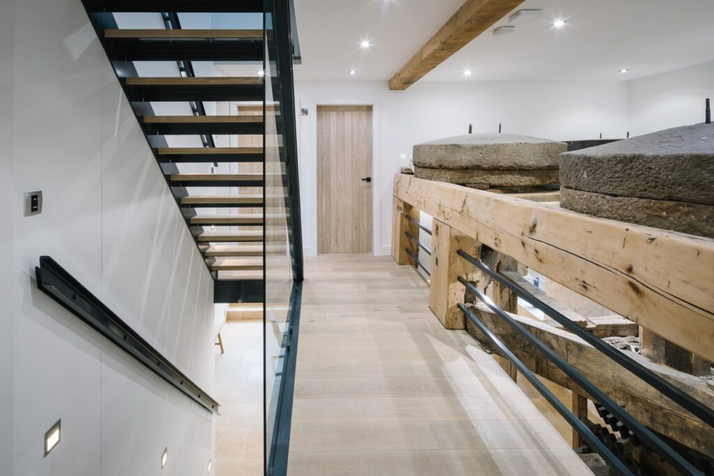 Bespoke commission of a three flights staircase with a juxtaposition of materials using a metal frame, wood treads and glass panelling. Bespoke lighting and matching metal handrail. Set against wood flooring.