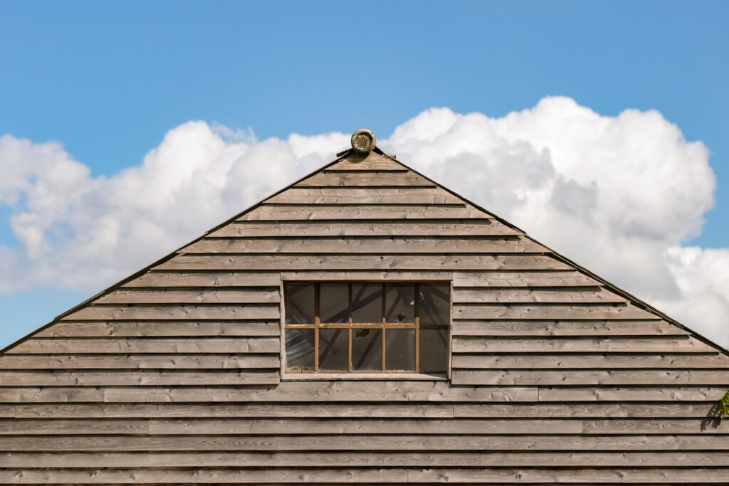 Gable end view of a shippon building with seasoned wood cladding and a wabi sabi broken window