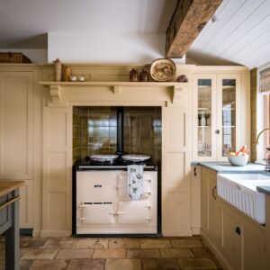 A bespoke farmhouse style kitchen, painted in a custom buttermilk paint colour. There is an Aga, double belfast sink and green slate worktops.