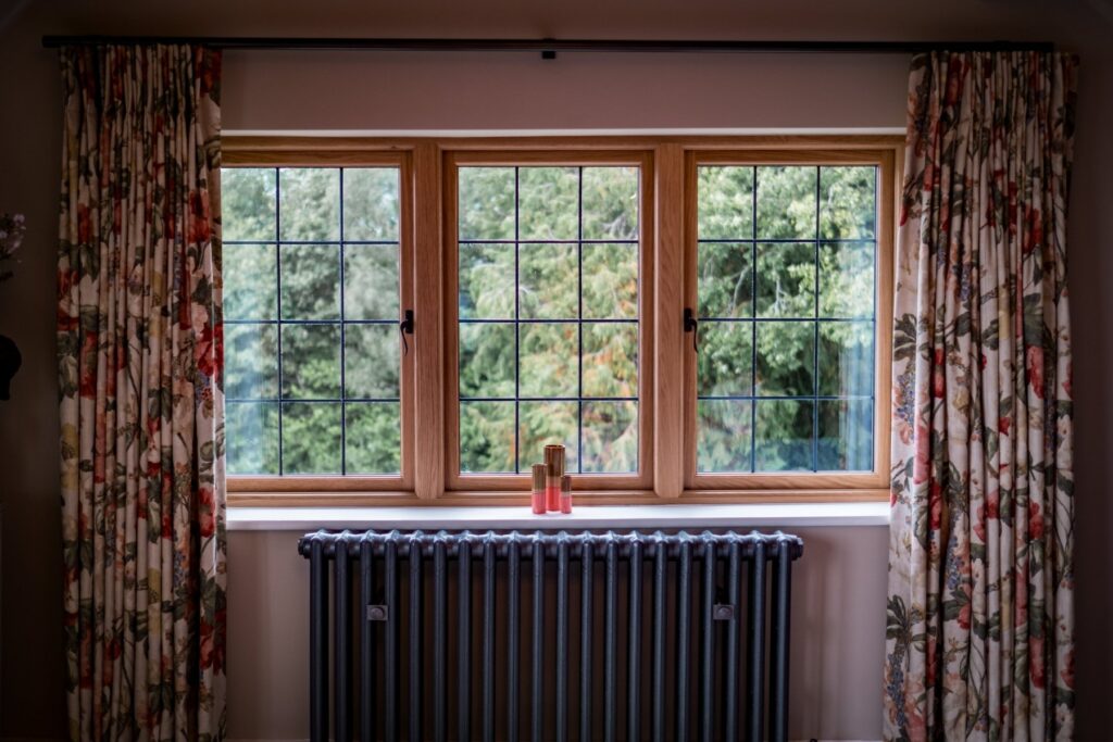 Looking out of a bedroom oak framed window, with a vintage radiator below the window and floral curtains pulled back.