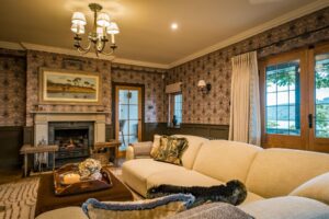 Arts & Crafts styling lounge, showing a decorative inset metal fireplace with natural stone surround, bespoke painted wood panelling, Performance linen sofa in an oatmeal textured weave and William Morris inspired wallpaper.