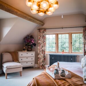 A principle bedroom with a super king bed with a natural wool throw draped, and a feature glass and metal large sphere cluster pendant