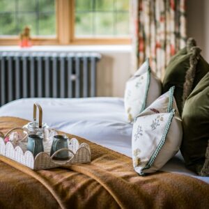 Close up of a super king bed with many cushions on it, a tea set on a tray and a natural throw draped