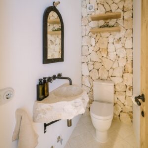 A loo with a feature natural stone back wall and a hand carved stone sink