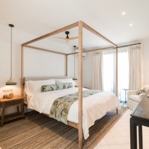 A guest bedroom with a feature wooden four poster bed, with hand made real leaf printed bed throw and cushion, in a light and airy room with marez stone flooring