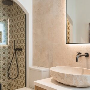 A glimpse through the ensuite door seeing the hand carved stone sink, the vanity mirror with its led lighting on and the edge of the walk in shower
