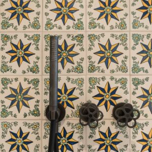 A close up of the shower hand held, round taps and the Menorcan hand made square tiles with an 8 pointed star in yellow and blue colours