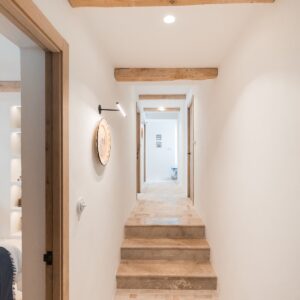 A lit hallway view which glimpses into the twin bedroom and also looks down the hallway with a focus on the marble steps and herringbone flooring