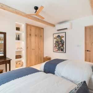 A twin bedroom with hand made wooden wardrobes, abstract wall art and an antique desk, mirror and chair in the corner by the full height windows