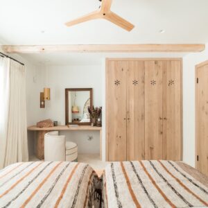 A twin bedroom with terracotta and beige bed linen, a hand made stone table with feature stone pillar, mirror and swivel chair in the corner and with hand made wooden wardrobes