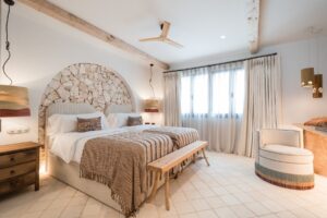 A twin bedroom with terracotta and beige bed linen, a recessed arch with a feature stone wall, lots of light from the windows