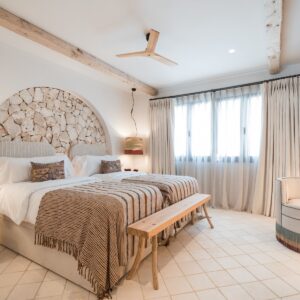 A twin bedroom with terracotta and beige bed linen, a recessed arch with a feature stone wall, lots of light from the windows