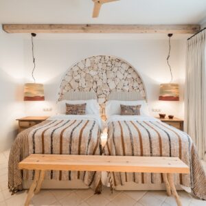 A front on view of the twin bedroom with terracotta and beige bed linen, a recessed arch with a feature stone wall, matching bedside tables and drop pendants