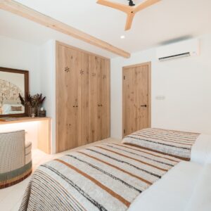 A twin bedroom with terracotta and beige bed linen, a hand made stone table with feature stone pillar, mirror and swivel chair in the corner and with hand made wooden wardrobes
