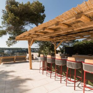 The outdoor terrace of a Menorcan Villa with a large pergola housing a fully furnished outdoor kitchen and bar area