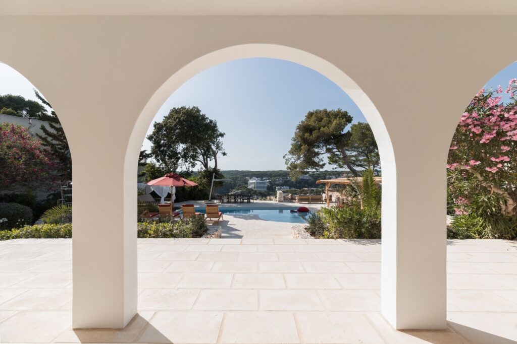 A view of the marez outdoor terrace, through the curved arch colonnade down to the pool of a Menorcan villa