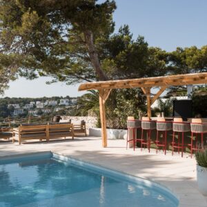 The outdoor terrace of a Menorcan Villa with a large pergola housing a fully furnished outdoor kitchen and bar area and a separate seating area for 8 to 10 people