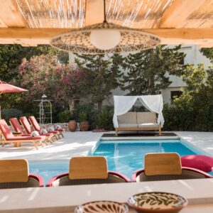 The view from inside a large pergola housing a fully furnished outdoor kitchen and bar area looking across the pool at the daybed and sun loungers at a Menorcan villa