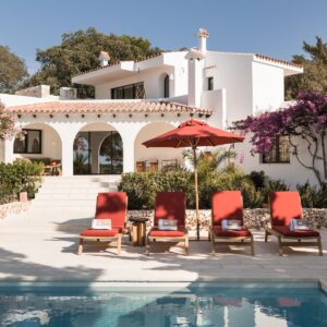 A view from the outdoor terrace looking back across the pool and sun loungers at the Menorcan villa with a terracotta tile roof and beautiful arched colonnade