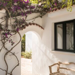 A close up on an external arch, with a rustic bench, framed with a mature bougainvillea at a Menorcan villa