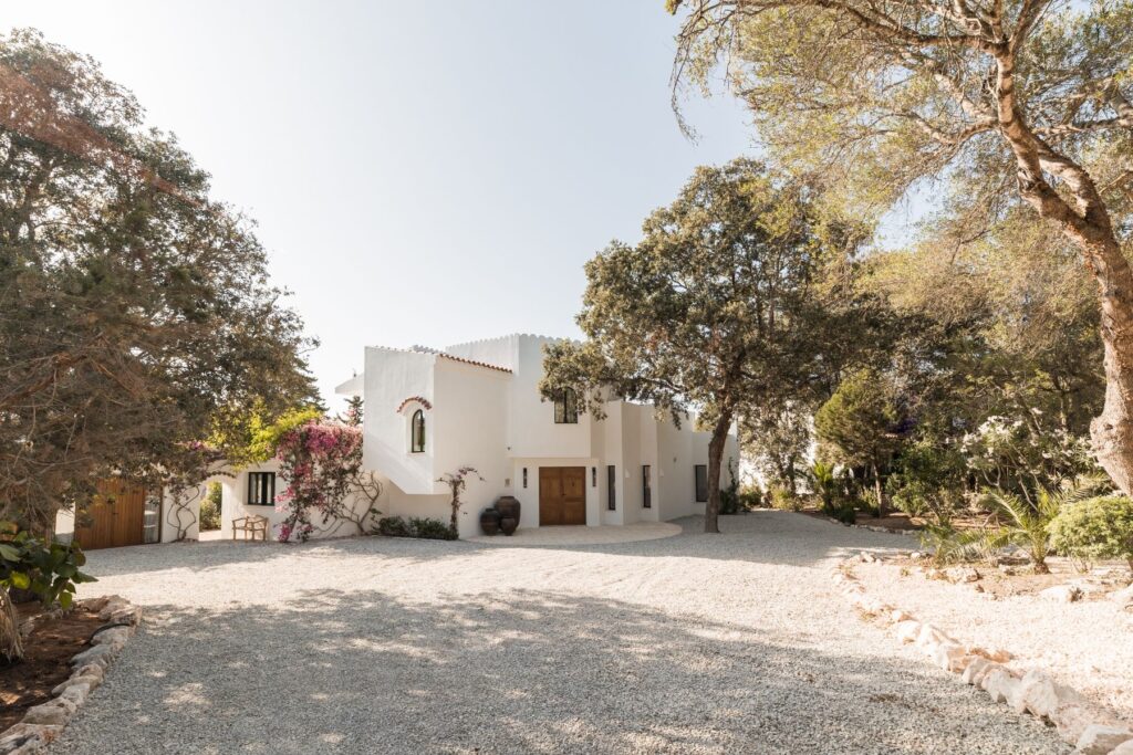 A wide angle view of a crisp white Menorcan villa, simple gravel driveway, with large pots outside the handmade entrance doors