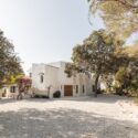 A wide angle view of a crisp white Menorcan villa, simple gravel driveway, with large pots outside the handmade entrance doors