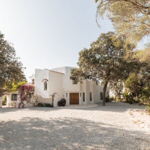 A wide angle view of a crisp white Menorcan villa, simple gravel driveway, with large pots outside the handmade entrance doors
