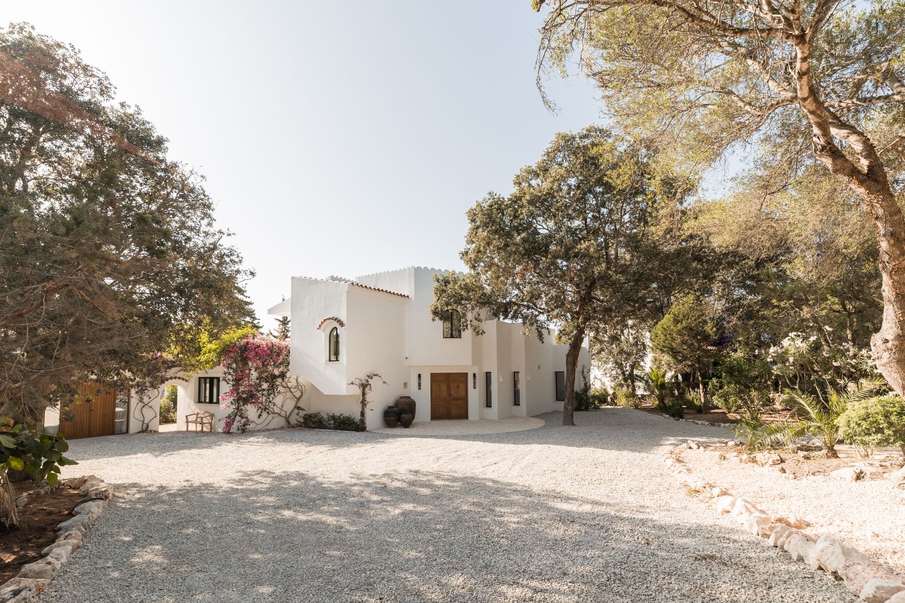 A wide angle view of a crisp white Menorcan villa, simple gravel driveway, with large pots outside the handmade entrance doors