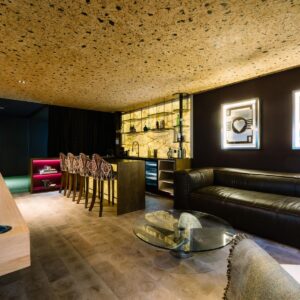 A luxury games room view across the custom pool table to the sofa relaxing area with large wall mounted metal car art pieces and a custom back lit stone wall bar.