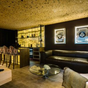 A luxury games room view across the custom pool table to the sofa relaxing area with large wall mounted metal car art pieces and a custom back lit stone wall bar.