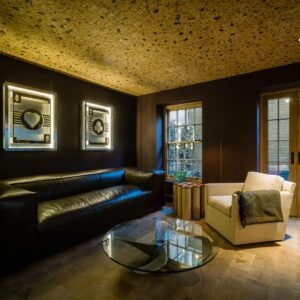 A luxury games room with natural wood flooring, cork ceiling, glass coffee table with an old junk ship propeller as the stand, large sofa and a single seat.