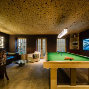 A luxury games room with natural wood flooring, cork ceiling, a custom pool table, a large wall mounted TV.